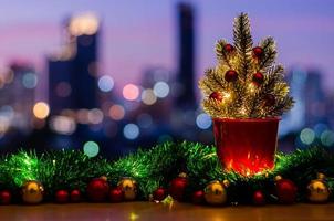 árbol de navidad decorado con adornos de adorno y luces en la mesa con fondo de luces de ciudad coloridas. foto