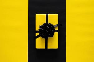 A yellow gift box with black ribbon puts on black and yellow background. Black friday and Boxing day concept. photo