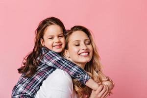 mujer adulta y niña abrazándose y sonriendo contra un fondo rosa. retrato de una mamá positiva foto