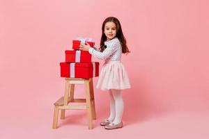 Cute curly girl in fluffy skirt and polka dot blouse takes box with gift. Female child posing on pi photo