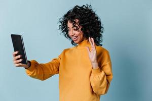 Ecstatic girl waving hand during video call. Happy mixed race woman using digital tablet. photo