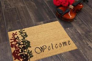 New Delhi, Delhi, IN, 2022 - Beautiful cursive welcome peach color doormat with red and black flower plant placed on brown floor with Guitar photo