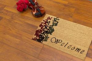 New Delhi, Delhi, IN, 2022 - Beautiful cursive welcome peach color doormat with red and black flower plant placed on brown floor with Guitar photo