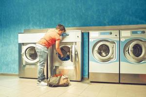 A girl fills up a public automatic washing machines with dirty cloths photo