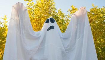 Halloween ghost, dancing in the autumn yellow forest, waving his hands. A merry ghost in a white sheet. photo