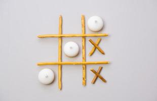 tic-tac-toe from crackers and sticks on a gray background. Food concept. Edible snacks dry sticks with salt and cookies on a white plate. Straws, sticks for crackers. photo