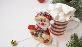Traditional hot chocolate with marshmallows and a snowman on a white textured background. Christmas drink theme. photo