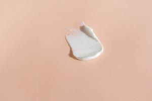 White smear of cosmetic cream on a beige background. Creamy foundation texture isolated. Smear of face cream. Close up of cream texture photo