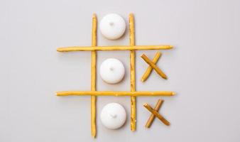 Creative mockup of tic-tac-toe game made from crackers and cookies sticks on gray background. Food concept. Edible snacks dry sticks with salt and cookies on a white plate. Straws, crackers sticks. photo