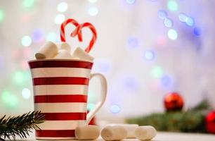 Hot cocoa with marshmallows and red-white lollipop. Hot chocolate with marshmallows in a New Year's cup against a background of multi-colored bokeh. photo