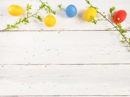 Colorful Easter eggs with spring bloom flowers and green leaves, on a white wooden background. Space for text. photo