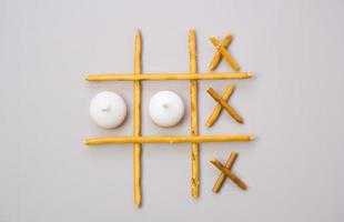 tic-tac-toe from crackers and sticks on a beige background. Food concept. Edible snacks dry sticks with salt and cookies on a white plate. Straws, sticks for crackers. photo