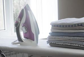 Stack of clean clothes and electric iron on board photo