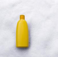 Mockup of a yellow plastic tube with moisturizer, shower gel, shampoo or facial cleanser and gentle soap suds with bubbles on a white background, top view. photo