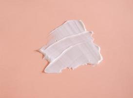 White smear of cosmetic cream on a beige background. Creamy foundation texture isolated. Smear of face cream. Close up of cream texture photo