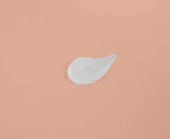 White smear of cosmetic cream on a beige background. Creamy foundation texture isolated. Smear of face cream. Close up of cream texture photo