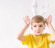 niño feliz en una camiseta amarilla en orejas de conejo sobre un fondo blanco. feliz concepto de pascua con lugar para el texto. foto