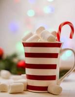 Hot cocoa with marshmallows and red-white lollipop. Hot chocolate with marshmallows in a New Year's cup against a background of multi-colored bokeh. photo