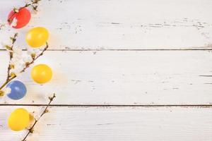 Colorful Easter eggs with spring bloom flowers and green leaves, on a white wooden background. Space for text. photo