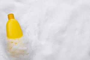 Mockup of a yellow plastic tube with moisturizer, shower gel, shampoo or facial cleanser and gentle soap suds with bubbles on a white background, top view. photo