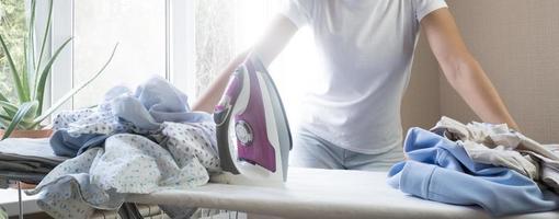 Frustrated tired young woman holds stares at iron and pile of ironed clothes at home. Housework photo