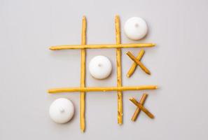 tic-tac-toe from crackers and sticks on a gray background. Food concept. Edible snacks dry sticks with salt and cookies on a white plate. Straws, sticks for crackers. photo