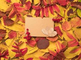 Hola octubre. composición otoñal, vista superior de hojas otoñales de colores brillantes con una hoja de papel y dos corazones de madera. espacio para texto foto