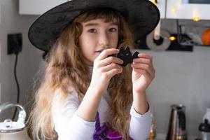 Child decorates the kitchen in home for Halloween. Girl in a witch costume plays with the decor for the holiday - bats, jack lantern, pumpkins. Autumn comfort in house, Scandi-style kitchen, loft photo