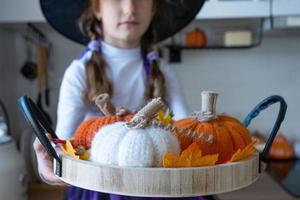 Child decorates the kitchen in home for Halloween. Girl in a witch costume plays with the decor for the holiday - bats, jack lantern, pumpkins. Autumn comfort in house, Scandi-style kitchen, loft photo