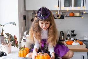 Child decorates the kitchen in home for Halloween. Girl in a witch costume plays with the decor for the holiday - bats, jack lantern, pumpkins. Autumn comfort in house, Scandi-style kitchen, loft photo