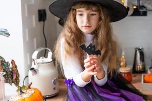 niño decora la cocina en casa para halloween. una chica disfrazada de bruja juega con la decoración de las vacaciones: murciélagos, farolillos, calabazas. comodidad otoñal en casa, cocina de estilo escandinavo, loft foto