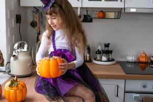 Child decorates the kitchen in home for Halloween. Girl in a witch costume plays with the decor for the holiday - bats, jack lantern, pumpkins. Autumn comfort in house, Scandi-style kitchen, loft photo