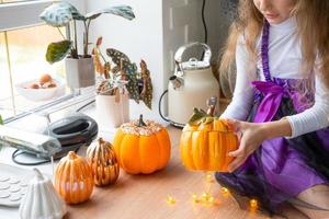 niño decora la cocina en casa para halloween. una chica disfrazada de bruja juega con la decoración de las vacaciones: murciélagos, farolillos, calabazas. comodidad otoñal en casa, cocina de estilo escandinavo, loft