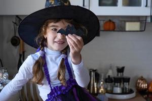 niño decora la cocina en casa para halloween. una chica disfrazada de bruja juega con la decoración de las vacaciones: murciélagos, farolillos, calabazas. comodidad otoñal en casa, cocina de estilo escandinavo, loft foto