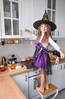 Child decorates the kitchen in home for Halloween. Girl in a witch costume plays with the decor for the holiday - bats, jack lantern, pumpkins. Autumn comfort in house, Scandi-style kitchen, loft photo