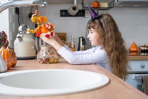 Child decorates the kitchen in home for Halloween. Girl in a witch costume plays with the decor for the holiday - bats, jack lantern, pumpkins. Autumn comfort in house, Scandi-style kitchen, loft photo