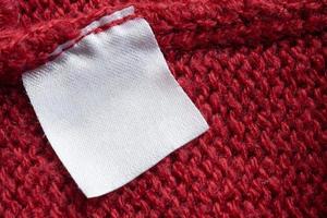 Blank laundry care clothes label on red knitted fabric texture background photo