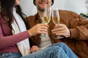 Couple celebrating holiday at home together. Sitting on sofa in sweaters and drinking champagne photo