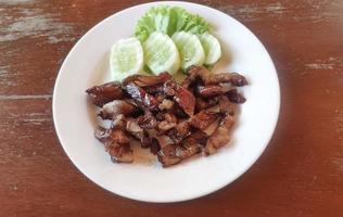 Grilled marinated barbecue pork neck with seasoned sauce on white plate with cucumber on the side. Asian Thai street food concept. photo