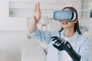 Disabled girl in virtual reality glasses experiencing augmented reality, using bionic prosthetic arm photo