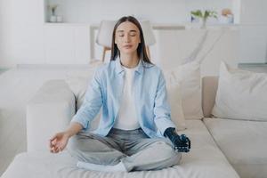 Calm disabled girl does yoga with bionic prosthesis arm at home. Healthy lifestyle and disability photo