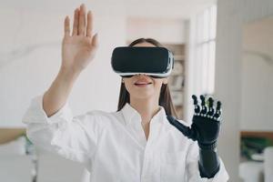Girl in VR glasses interacts with augmented reality, touches virtual object by bionic prosthetic arm photo