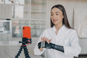 Young disabled girl blogger records video on smartphone talking about bionic prosthetic arm at home photo