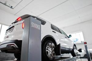 coche todoterreno americano en soporte para verificación de inclinación de alineación de ruedas en el taller de la estación de servicio. foto