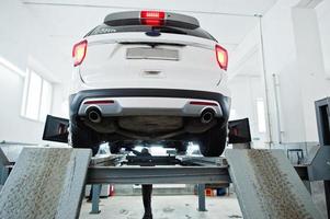 coche todoterreno americano en soporte para verificación de inclinación de alineación de ruedas en el taller de la estación de servicio. foto