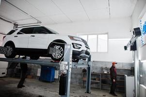 coche todoterreno americano en soporte para verificación de inclinación de alineación de ruedas en el taller de la estación de servicio. foto