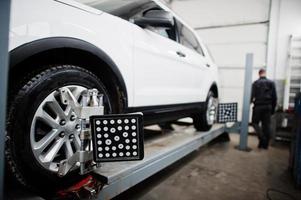 coche todoterreno americano en soporte para verificación de inclinación de alineación de ruedas en el taller de la estación de servicio. foto