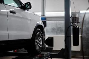 coche todoterreno americano en soporte para verificación de inclinación de alineación de ruedas en el taller de la estación de servicio. foto