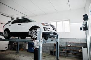 coche todoterreno americano en soporte para verificación de inclinación de alineación de ruedas en el taller de la estación de servicio. foto