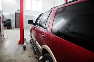 coche todoterreno americano en soporte para verificación de inclinación de alineación de ruedas en el taller de la estación de servicio. foto